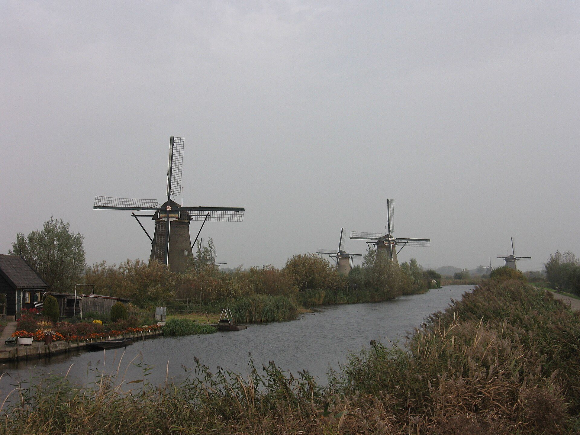 A line of windmills standing over flat water under an overcast sky